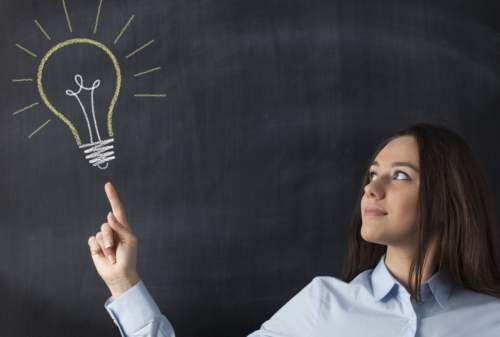 Big glowing light bulb on blackboard with businesswoman hand pointing it